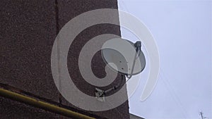 Satellite receiver dish on the wall with a cloudy sky and cloud behind