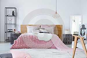 Satin beige pillows and fury white blanket on big warm bed in stylish bedroom interior, copy space on empty white wall