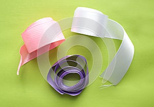 Satin ribbons for For decoration or sewing on green background. satiny tape. Pink, white, lilac. top view.