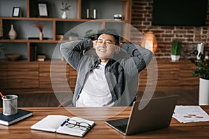 Satisfied adult japanese man resting in chair at table in office interior