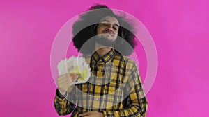 Satisfied African American man holding fan of money banknotes in his hands and looking at camera while standing isolated