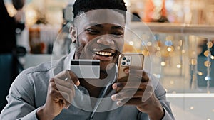 Satisfied african american man makes purchase in online store pays for goods with credit card on mobile phone uses e