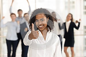 Satisfied african female showing thumbs up happy employees in background