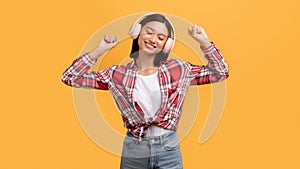 Satisfied asian lady in wireless headphone dancing, enjoying free time, listening music, isolated on yellow background