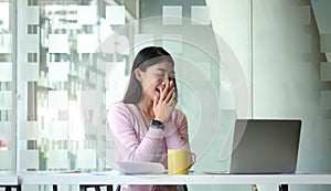 Satisfied asian young woman relaxing at her workplace and looking through the window at office