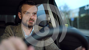 Satisfied bearded man driving a car down the street in sunny weather