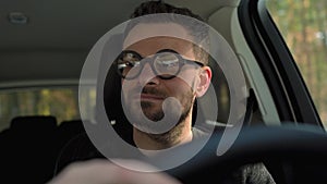 Satisfied bearded man in glasses driving a car down the street in sunny weather