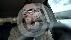 Satisfied bearded man in glasses driving a car down the street in sunny weather