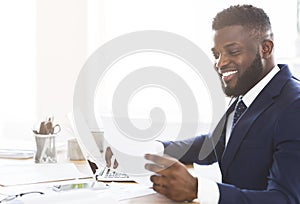 Satisfied black businessman checking reports, sitting in modern office