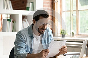 Satisfied businessman in glasses reading letter, working with correspondence