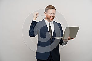 Satisfied businessman with laptop rejoicing prosperous business, successful deal isolated gray wall