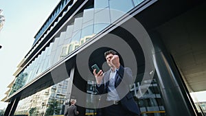 Satisfied businessman talking cell phone leaving office building. Happy manager