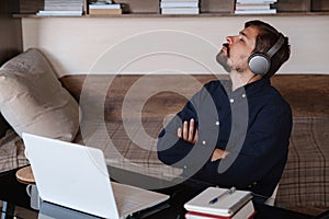 Satisfied businessman wearing headphones enjoying music at home