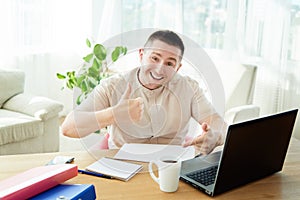 Satisfied businessman with work done in office. Happy young man working on laptop while sitting at workingplace