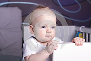 Satisfied and calm baby boy in his bed. An infant kid staying in a crib