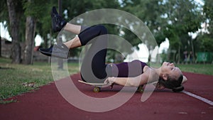 Satisfied Caucasian slim sportswoman lying on skateboard in spring summer park enjoying leisure after training. Live