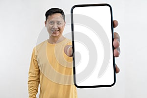 Satisfied confident smiling man showing mobile phone blank white screen mockup to camera standing isolated on studio copy space