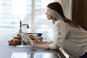 Satisfied cook girl holding mobile phone in kitchen, looking away