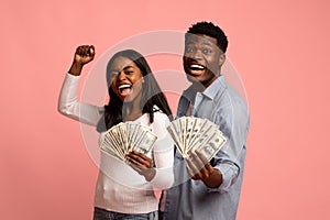 Satisfied couple holding bunch of money banknotes on pink