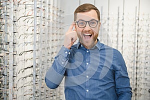 Satisfied Customer. View of happy young male client wearing new glasses, standing near rack and showcase with eyewear