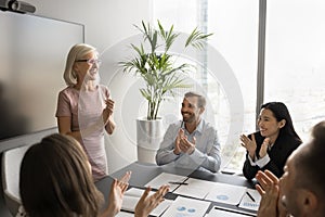 Satisfied diverse team of employees applauding mature female boss