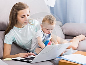 Satisfied female with child is productively working behind laptop