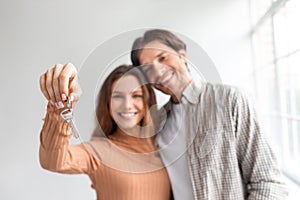 Satisfied glad young caucasian couple celebrate buying own apartment at loan, show keys in empty room