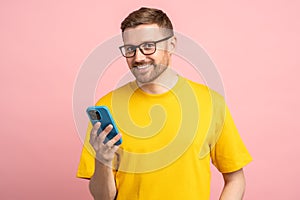 Satisfied with good news smiling bearded man in glasses looking at camera with mobile phone in hand