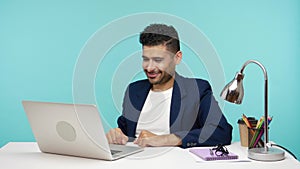 Satisfied happy business man in elegant suit pointing finger at laptop display and showing thumbs up, praising well done job