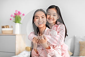 Satisfied happy cute teen girl hugging young japanese woman in pajama celebrating mother& x27;s day in bedroom