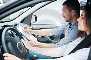 Satisfied male driving instructor notes results of test in his paper. Smiled man sitting on front passenger seat