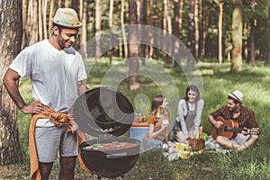 Joyous man cooking barbecue for friends in forest