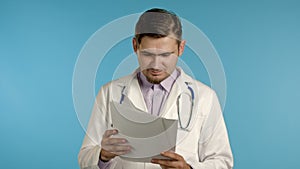 Satisfied man in professional medical coat holding files papers isolated on blue background. He nods his head