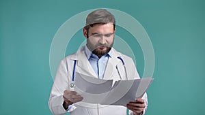 Satisfied man in professional medical coat holding files papers isolated on blue background. He nods his head