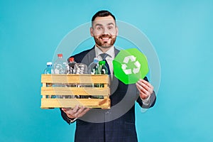 Satisfied man wearing official style suit holding box with plastic bottles and recycling green symbol, sorting his rubbish, saving