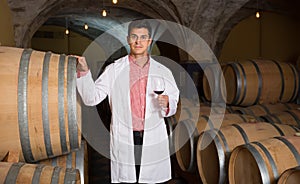 Satisfied man in white robe checking ageing process of red wine