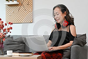 Satisfied mature woman reading online news, surfing internet on sofa at home