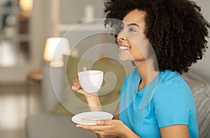 Satisfied millennial african american curly lady enjoy relax, cup of tea on sofa, look at copy space