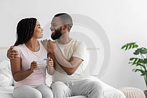 Satisfied millennial african american man look at cute woman hold positive pregnancy test, celebrate great news