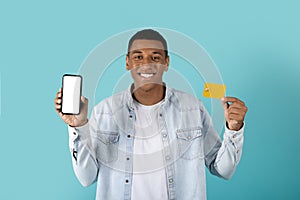 Satisfied millennial black guy shows credit card, phone with empty screen rejoice to win online
