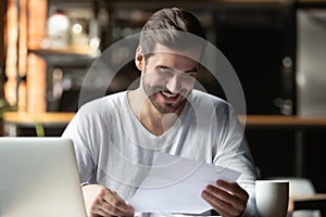 Satisfied millennial businessman reading paper letter with good news