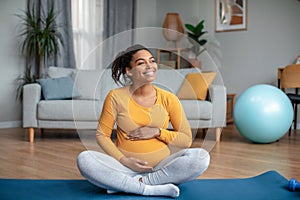 Satisfied millennial pregnant african american lady touching big belly feels movement of baby, practicing yoga