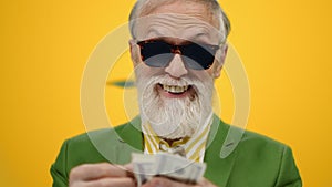 Satisfied old man staying under money rain. Mature guy counting dollars indoors.