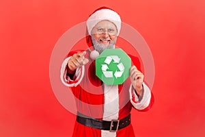 Satisfied positive elderly man with gray beard wearing santa claus costume pointing to camera with
