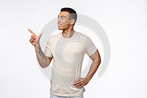 Satisfied and proud, smiling happy hispanic man with short haircut, tattoo, wear casual t-shirt, looking and pointing