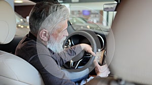 Satisfied senior car buyer talks to camera at steering wheel