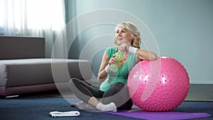 Satisfied senior female with bottle of water relaxing after workout, sport