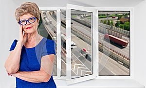 Satisfied senior woman standing near new triple-casement pvc window with loudy photo