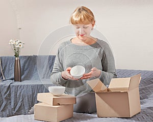 Satisfied shopper girl who received a purchase in an online store by postal delivery, unpacks the delivery and examines the goods