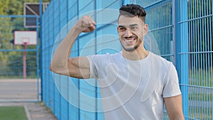 Satisfied sincere cheerful Arab bearded athletic guy in summer sportswear, showing off muscles, promises good results